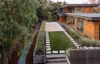 Modern house with a green lawn, concrete stepping stones, and a narrow canal lined with trees alongside the property.