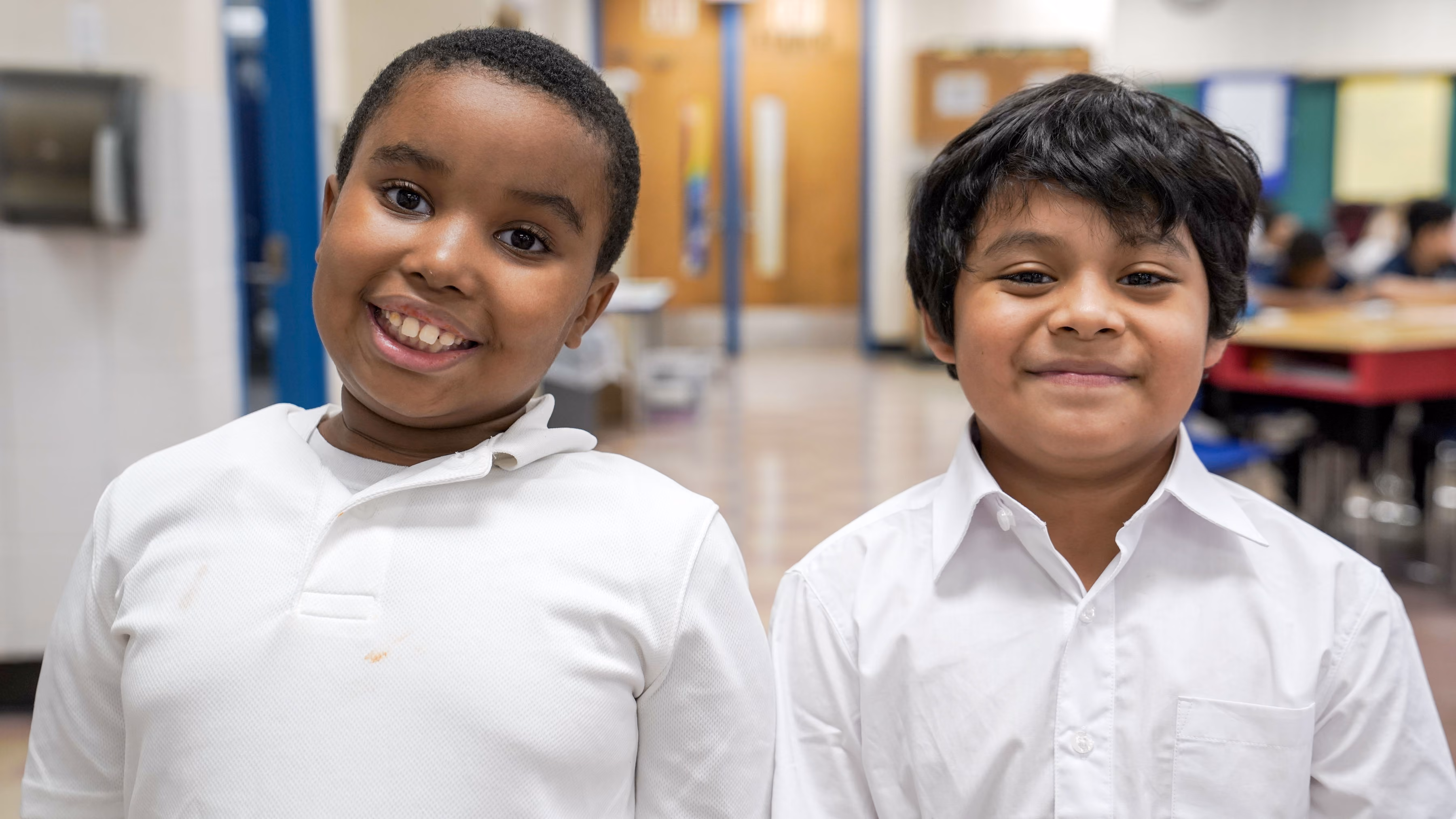 Two smiling elementary students in white shirts inside school
