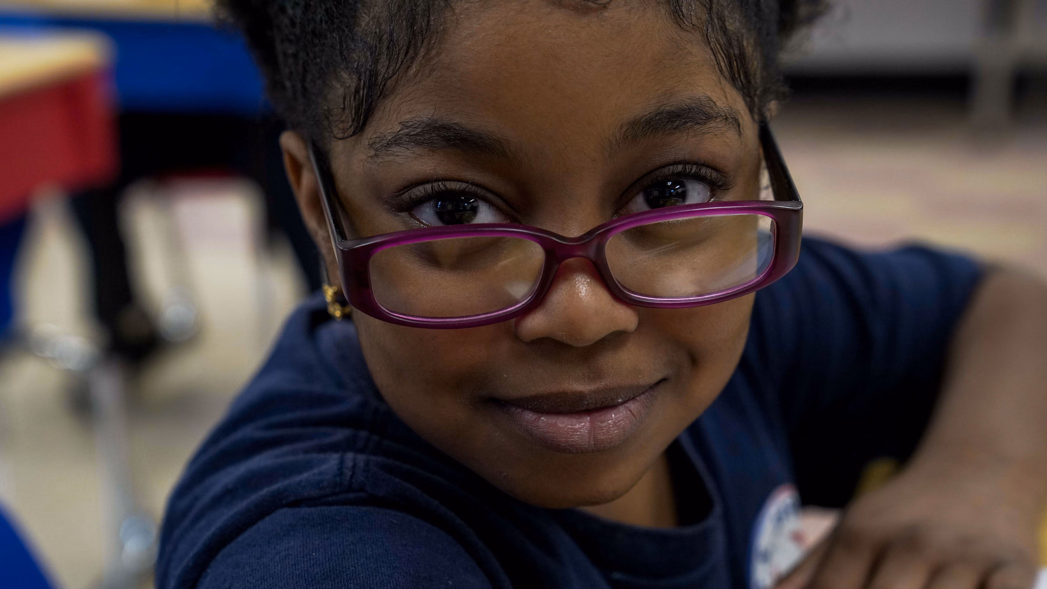 Smiling elementary student wearing pink glasses in classroom
