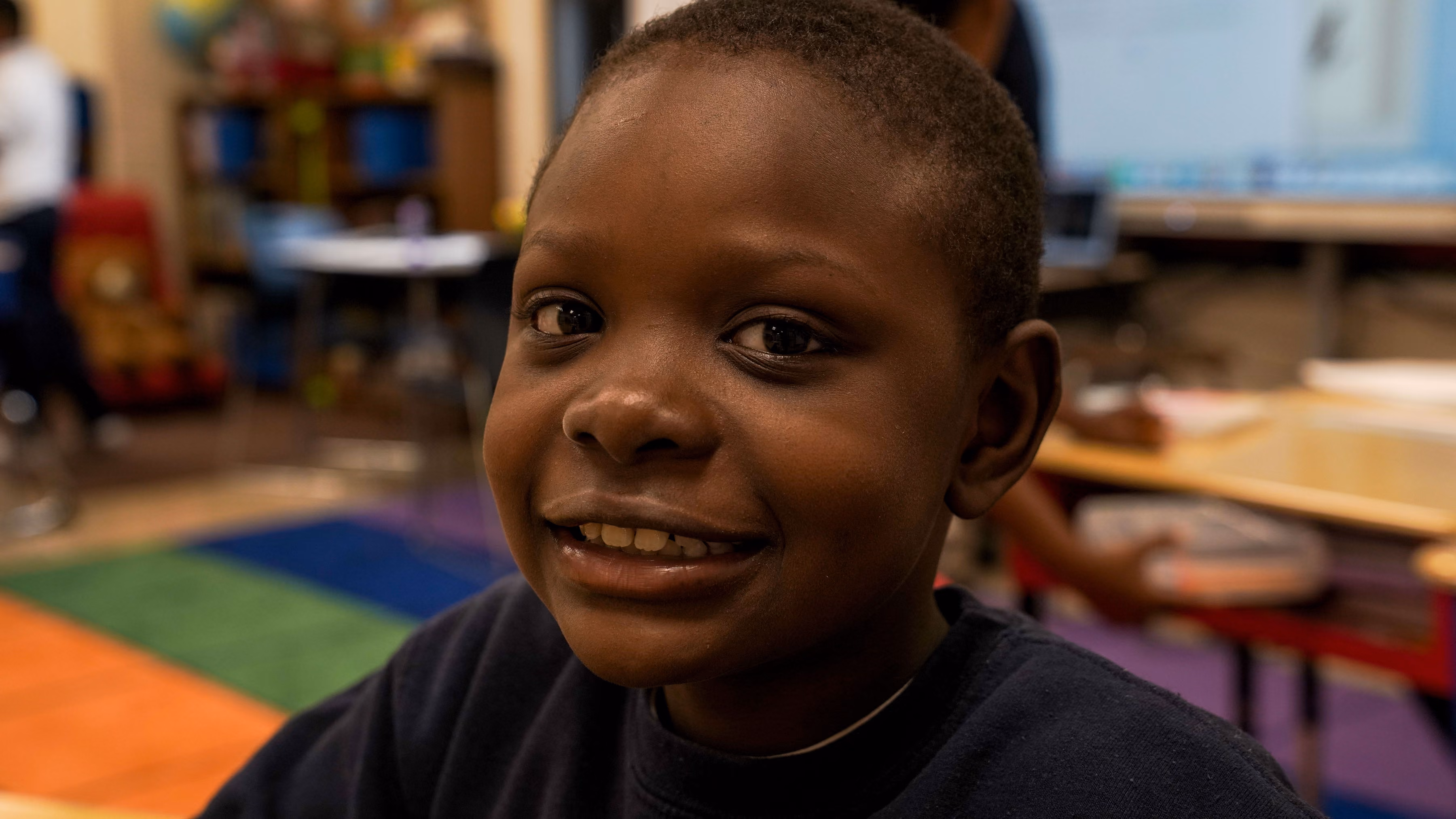 Smiling young student seated on a colorful classroom rug