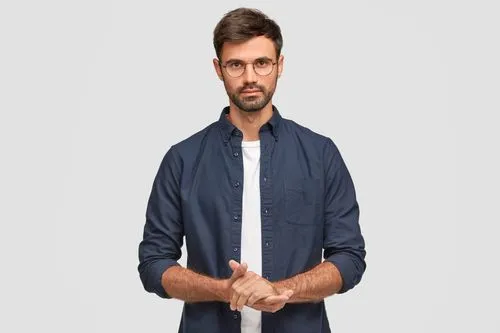 Man with glasses wearing a navy blue shirt over a white t-shirt, standing against a plain gray background.