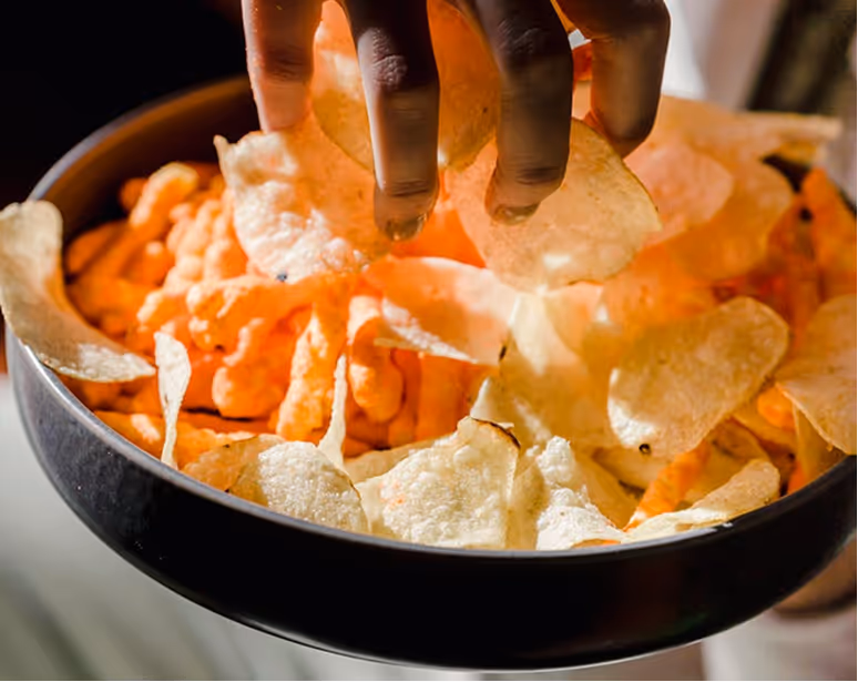 Multiple hands reaching into a bowl of baked potato chips.