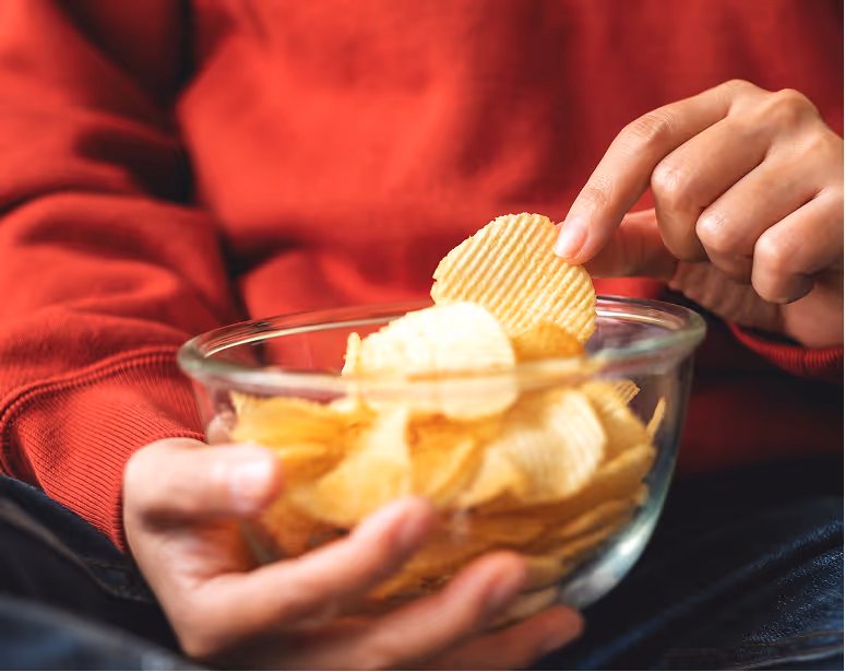 Person holding a bowl of baked potato chips while snacking.