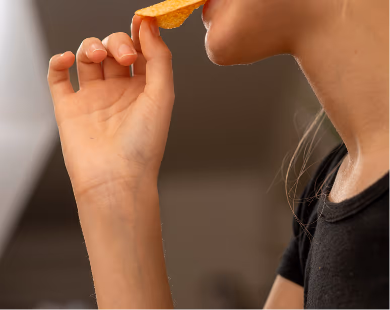 Profile view of a person eating a single baked potato chip.