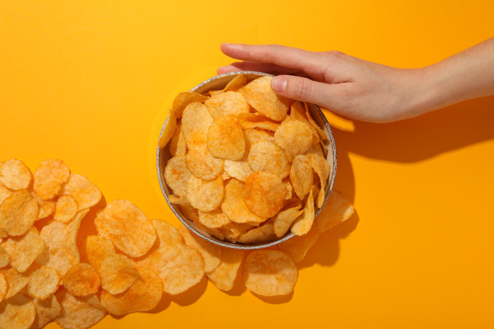 Hand reaching into a bowl filled with SNAXX baked potato chips.