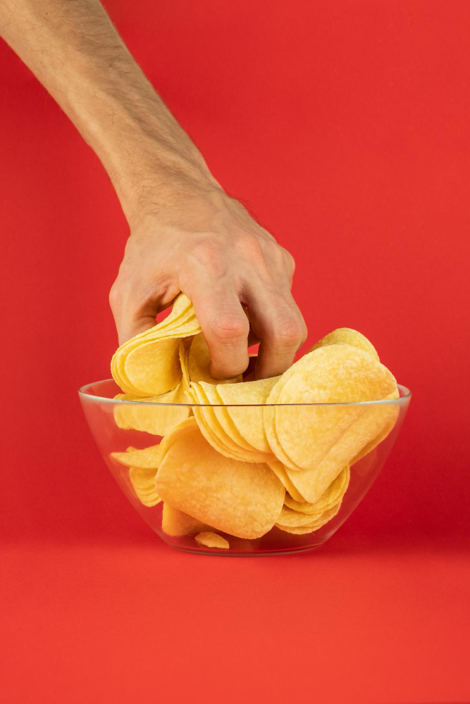 Hand grabbing baked potato chips against a red background.