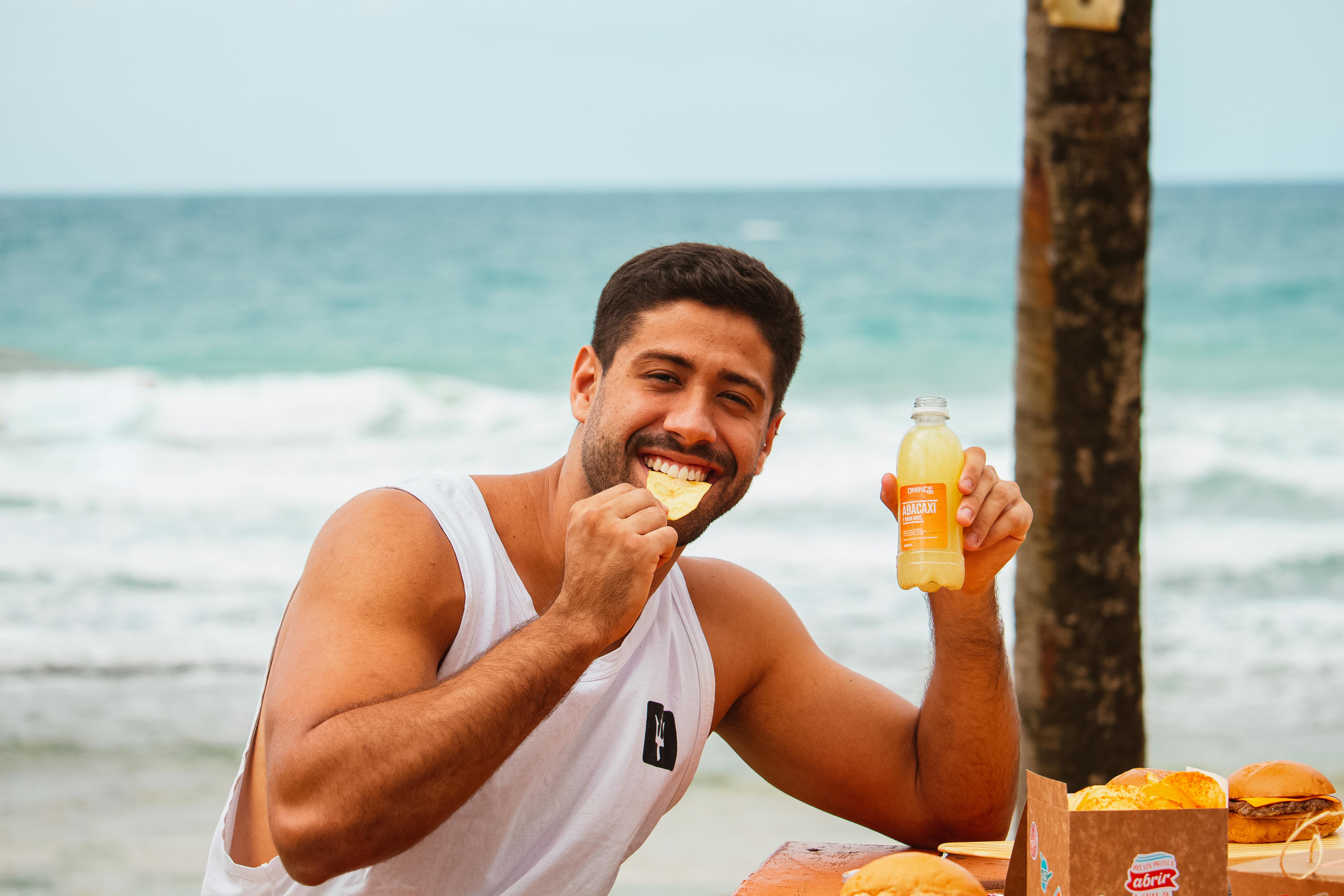 Man eating SNAXX baked potato chips outdoors near the beach.
