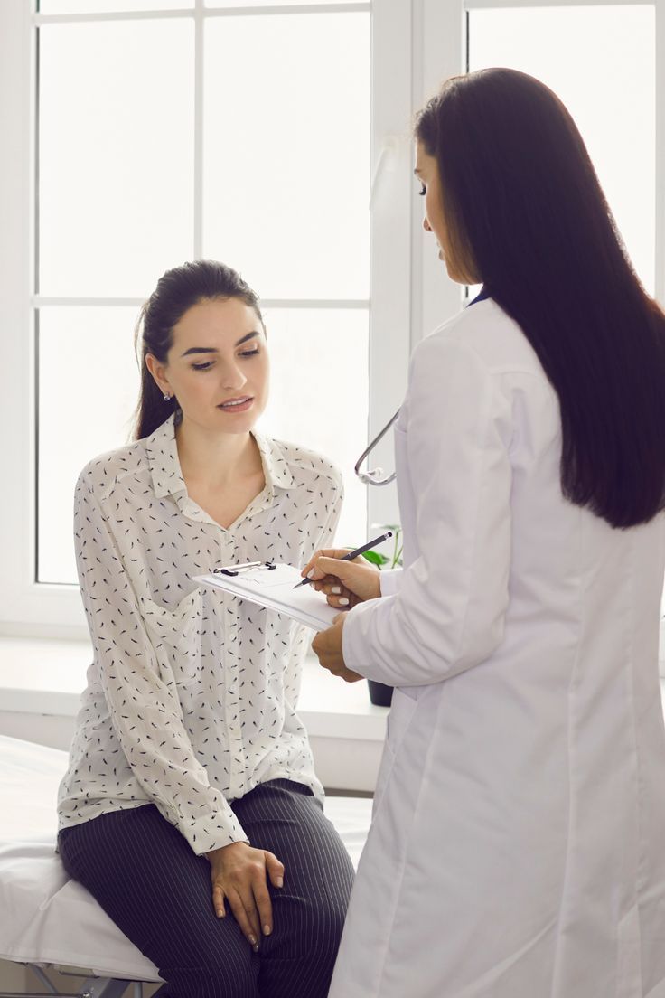 a female patient sitting on hospital bed nervously and a female doctor is standing in front of the patient holding a notepad, and explaining her options.