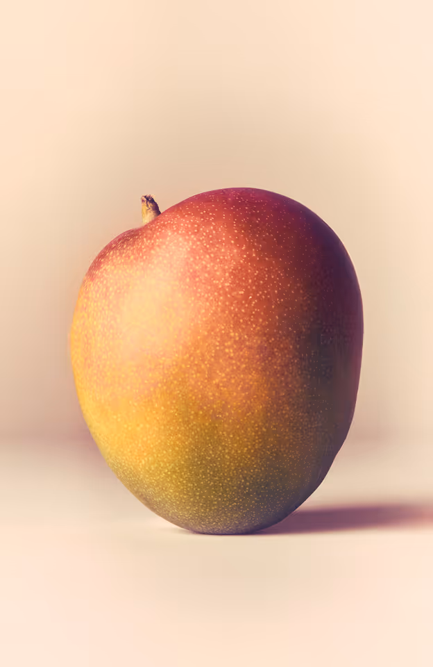 Ripe mango with red and yellow skin on a light background.