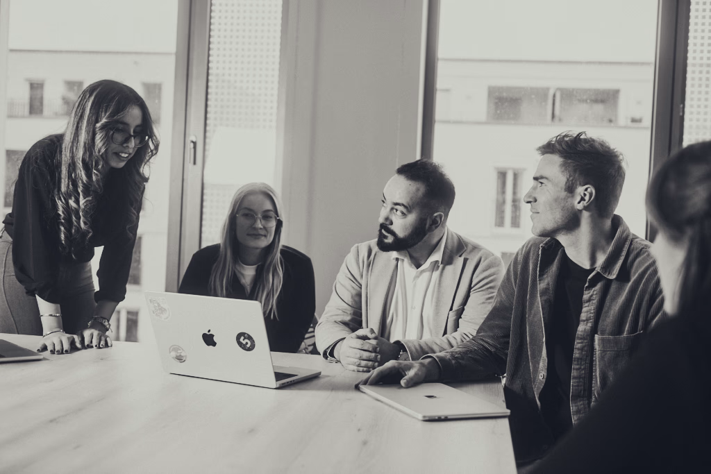 Group of four young adults engaged in a discussion in an office with large windows.