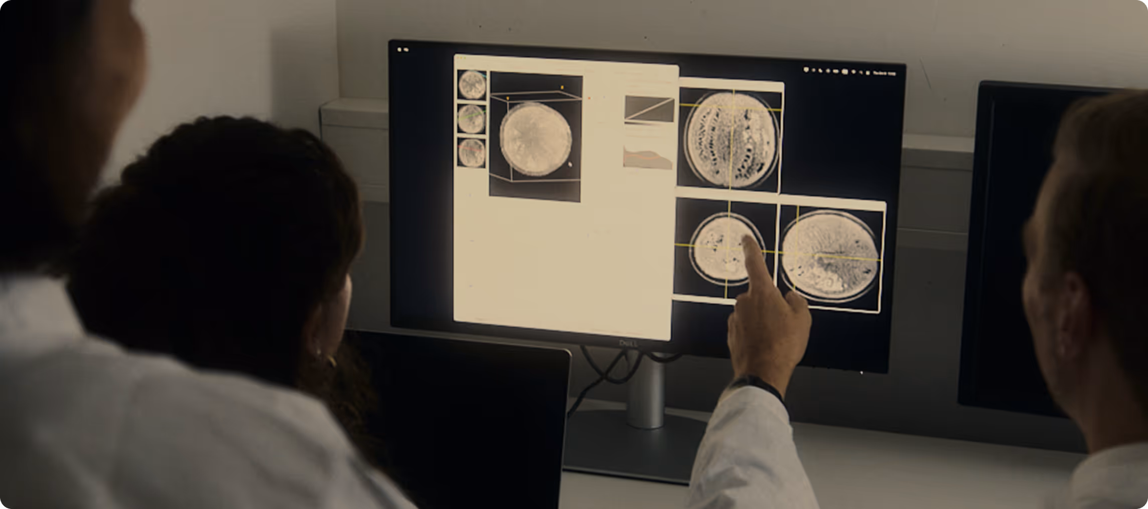 Three scientists in lab coats examining medical scan images displayed on a computer monitor.