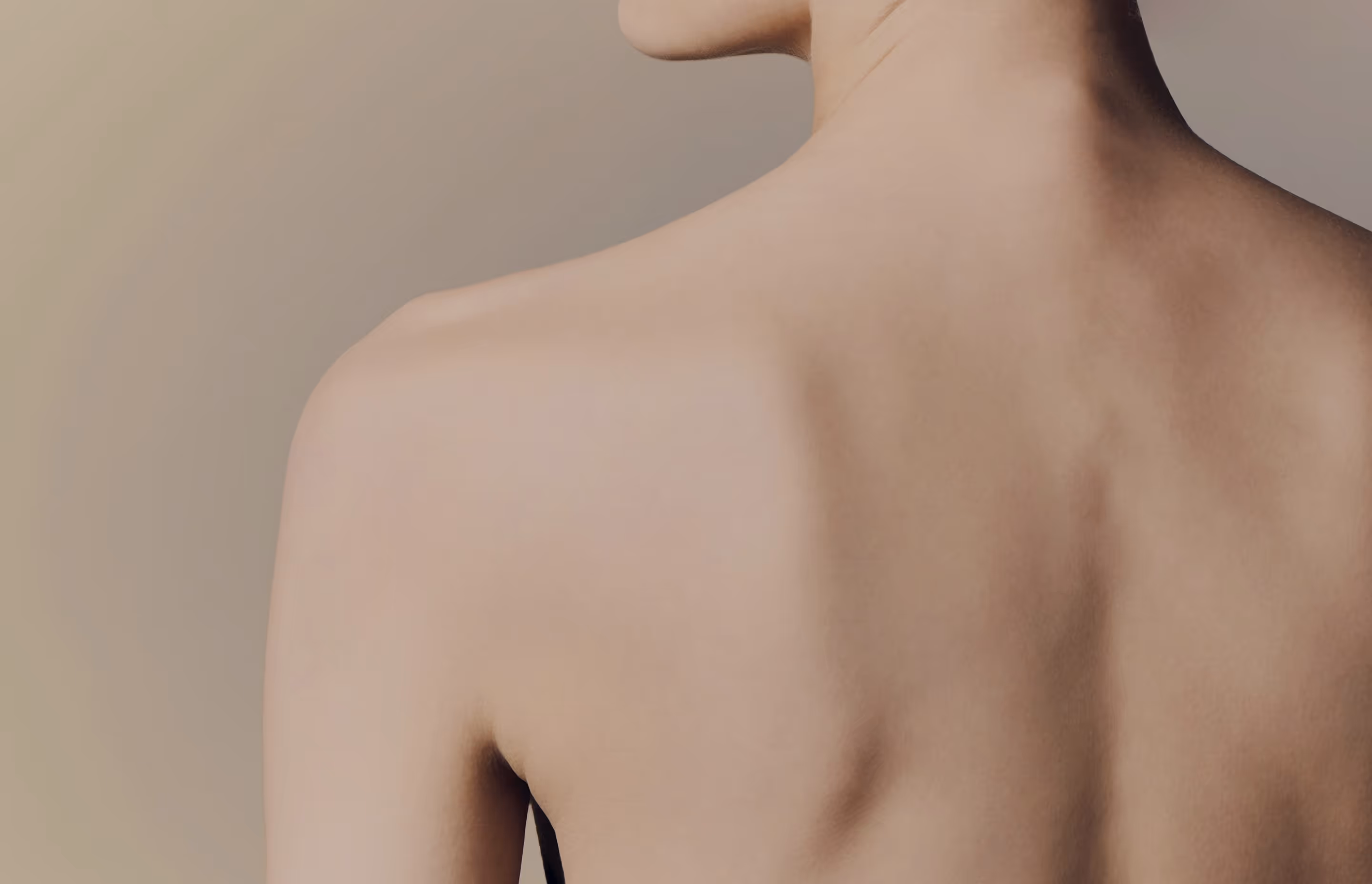 Close-up of a person's bare back and shoulder against a neutral background.