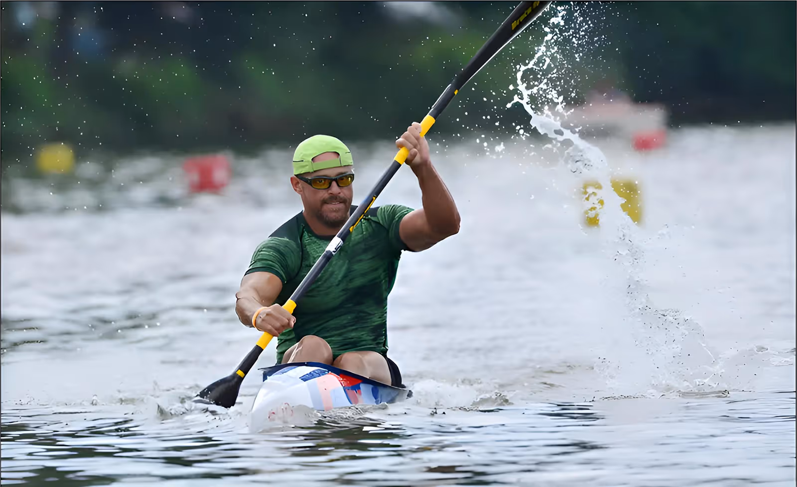Man paddling a kayak vigorously on a body of water with water splashing around the paddle.