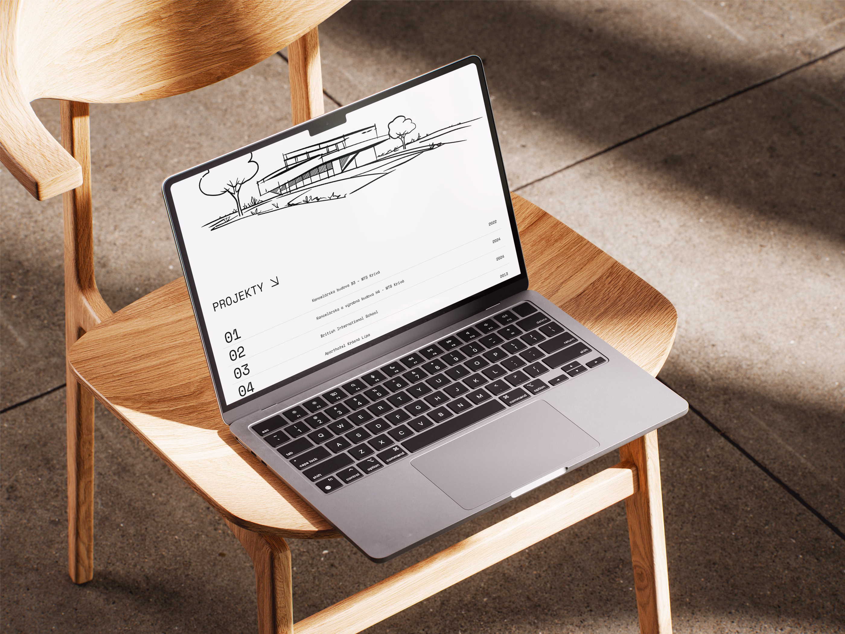 Silver laptop displaying an architectural project website with a sketch of a modern house and a project list, placed on a wooden chair on a tiled floor with sunlight and shadows.