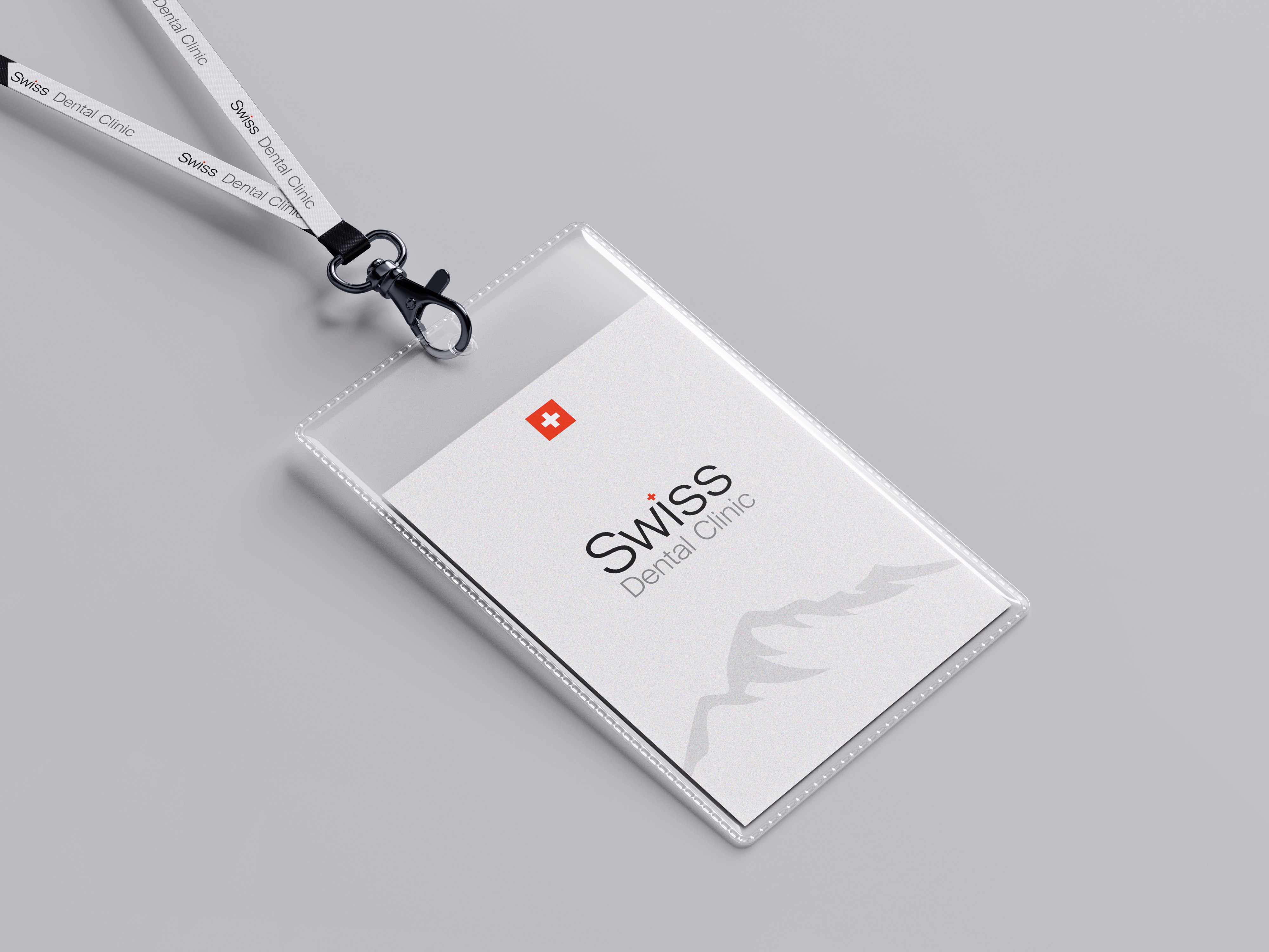 Clear plastic ID card holder with a white card inside displaying the logo 'Swiss Dental Clinic' featuring a red square with a white cross and a subtle mountain design, attached to a white lanyard with the text 'Swiss Dental Clinic'.