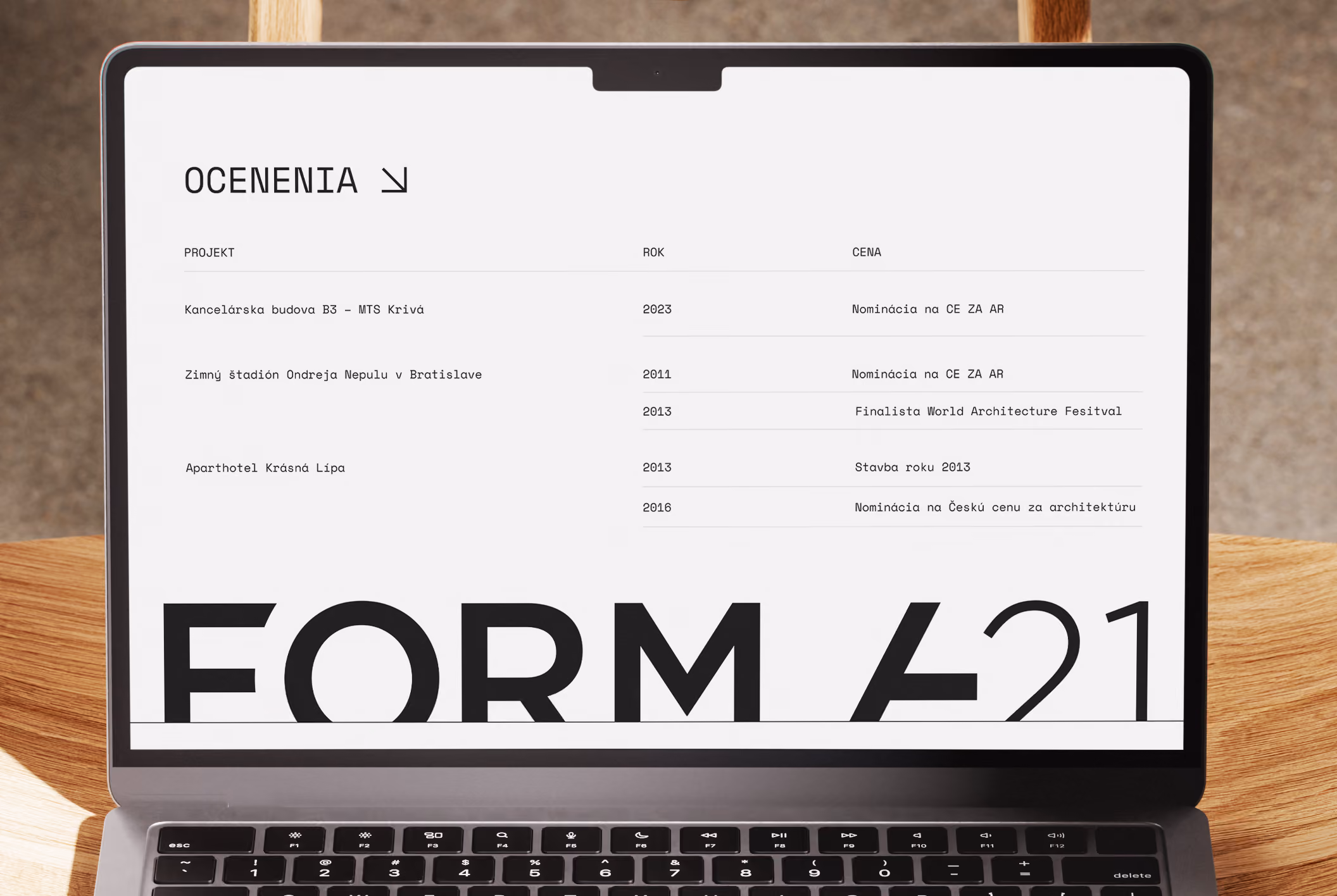 Laptop screen showing a list of architectural project awards with columns labeled Projekt, Rok, Cena, including projects like Kancelárska budova B3, Zimný štadión Ondreja Nepelu v Bratislave, and Aparthotel Krásná Lípa, with years 2011, 2013, 2016, and 2023, and awards such as Nominácia na CE ZA AR and Finalista World Architecture Festival.