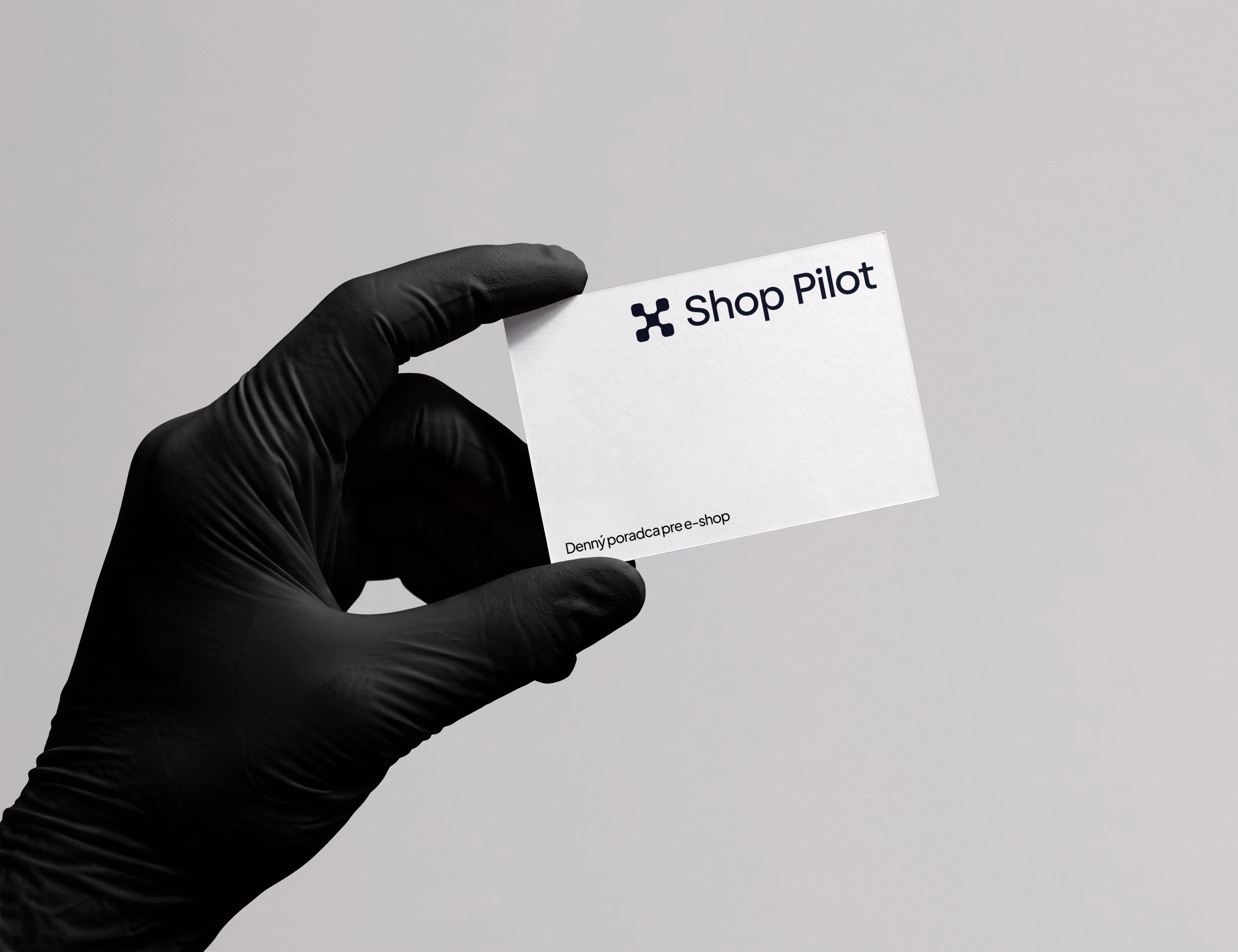 A hand wearing a black glove holding a business card with the Shop Pilot logo and the Slovak text 'Denný poradca pre e-shop' on a plain gray background.