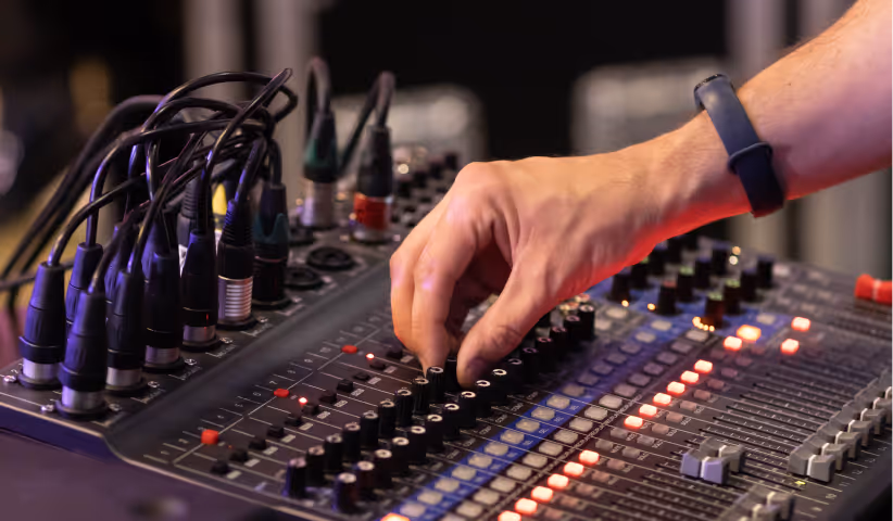 Close-up of a hand adjusting knobs on a sound mixing console with connected cables.