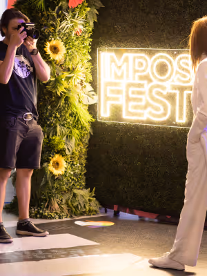 Photographer taking a photo of a woman standing near a neon sign and floral decoration.