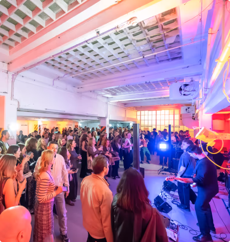 Crowded indoor concert venue with a band performing under colorful stage lights.
