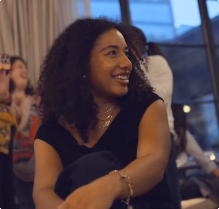 Smiling woman with curly hair sitting indoors during a social gathering.