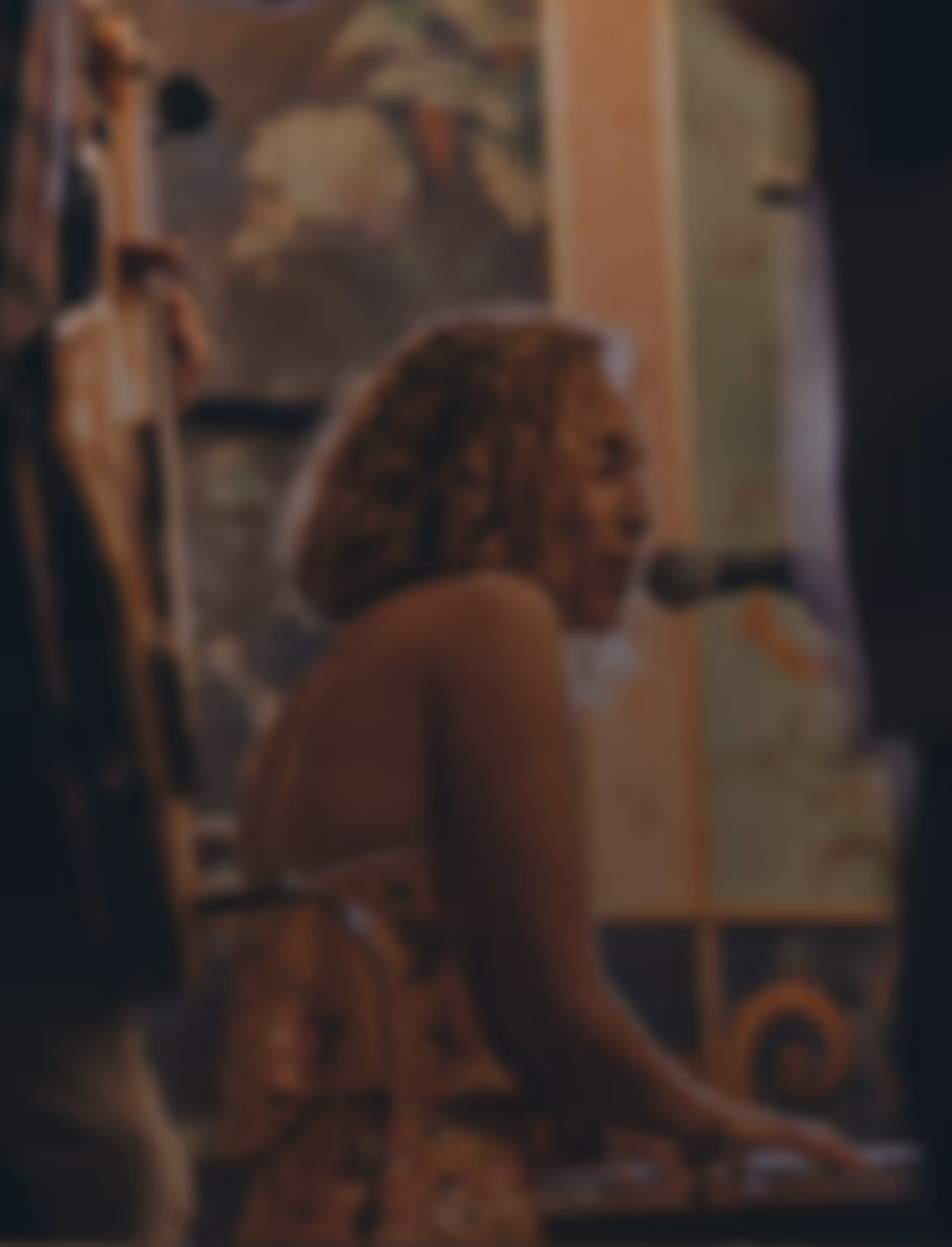 Blurred image of a woman singing into a microphone while playing a keyboard.