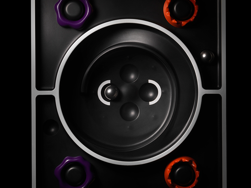 Close-up of a black tabletop labyrinth wooden game with small metal and wooden balls and purple and orange knobs.