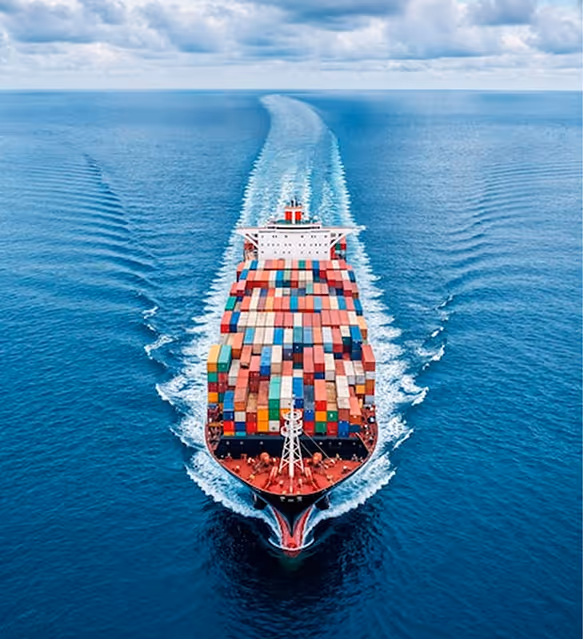 A large container ship loaded with colorful shipping containers sailing through calm blue ocean water under a cloudy sky.