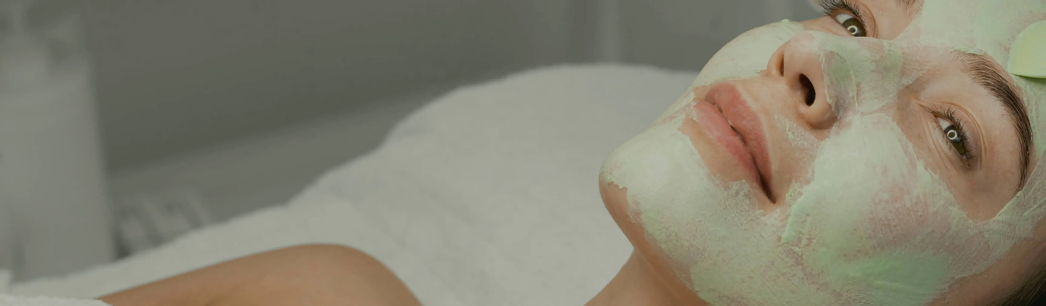 Close-up of a woman relaxing with a green facial mask applied on her face.