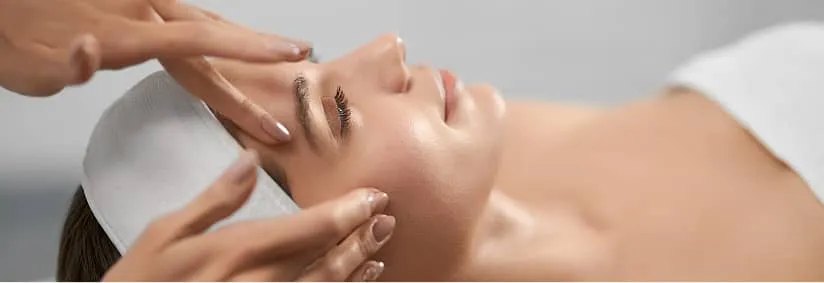 Woman receiving a facial massage with eyes closed and wearing a white headband.