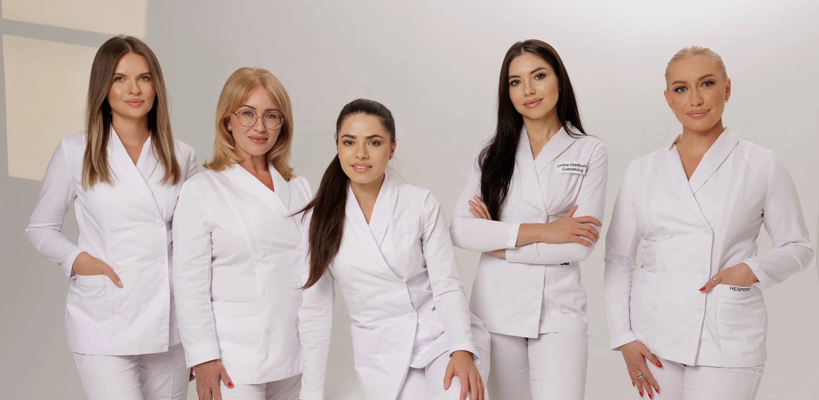 Five professional women in white medical jackets posing together against a light background.