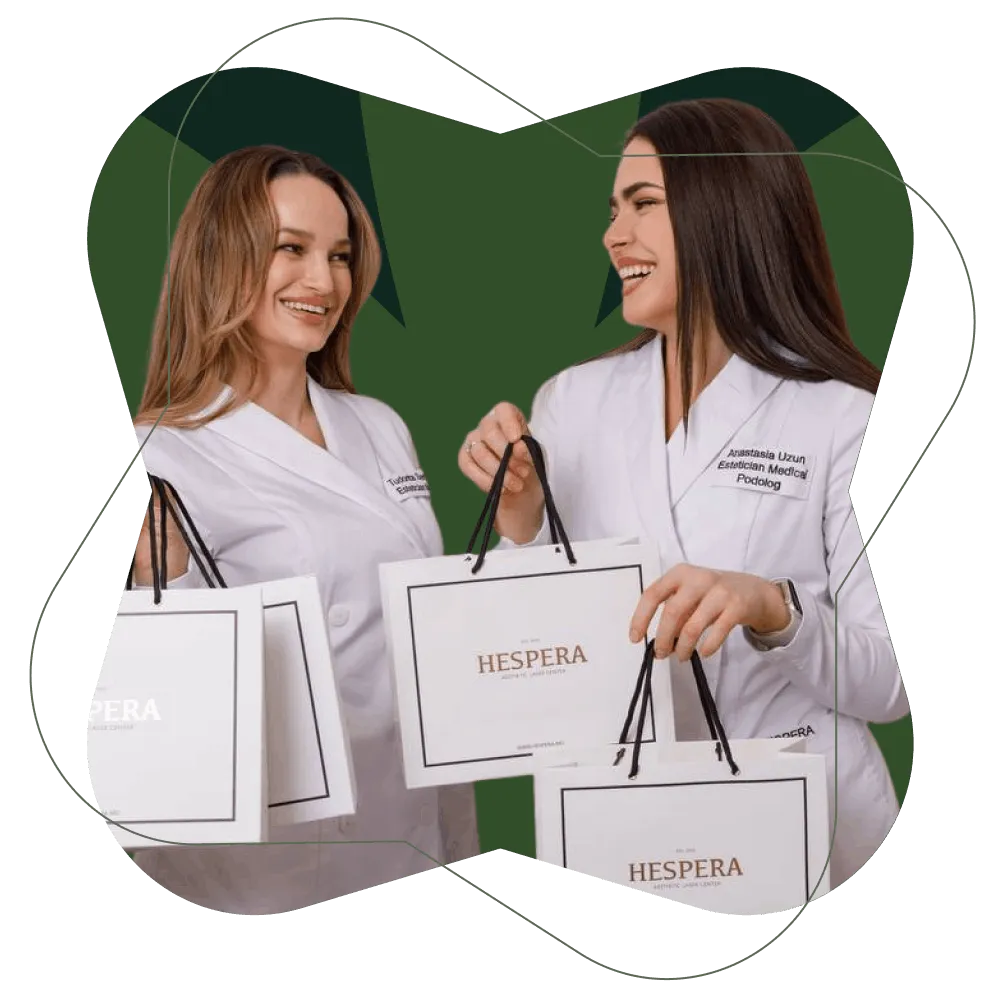 Two women in white medical coats holding white shopping bags with HESPERA Aesthetic Laser Center logo, smiling at each other.