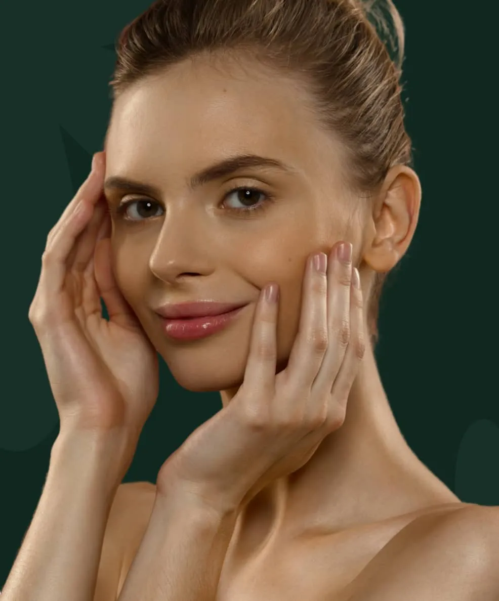 Young woman with clear skin gently touching her face, smiling slightly against a dark green background.