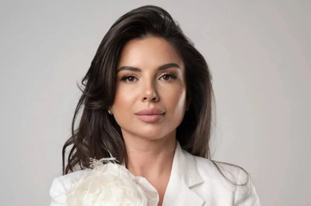 Portrait of a woman with long dark hair wearing a white blazer and holding a large white flower.
