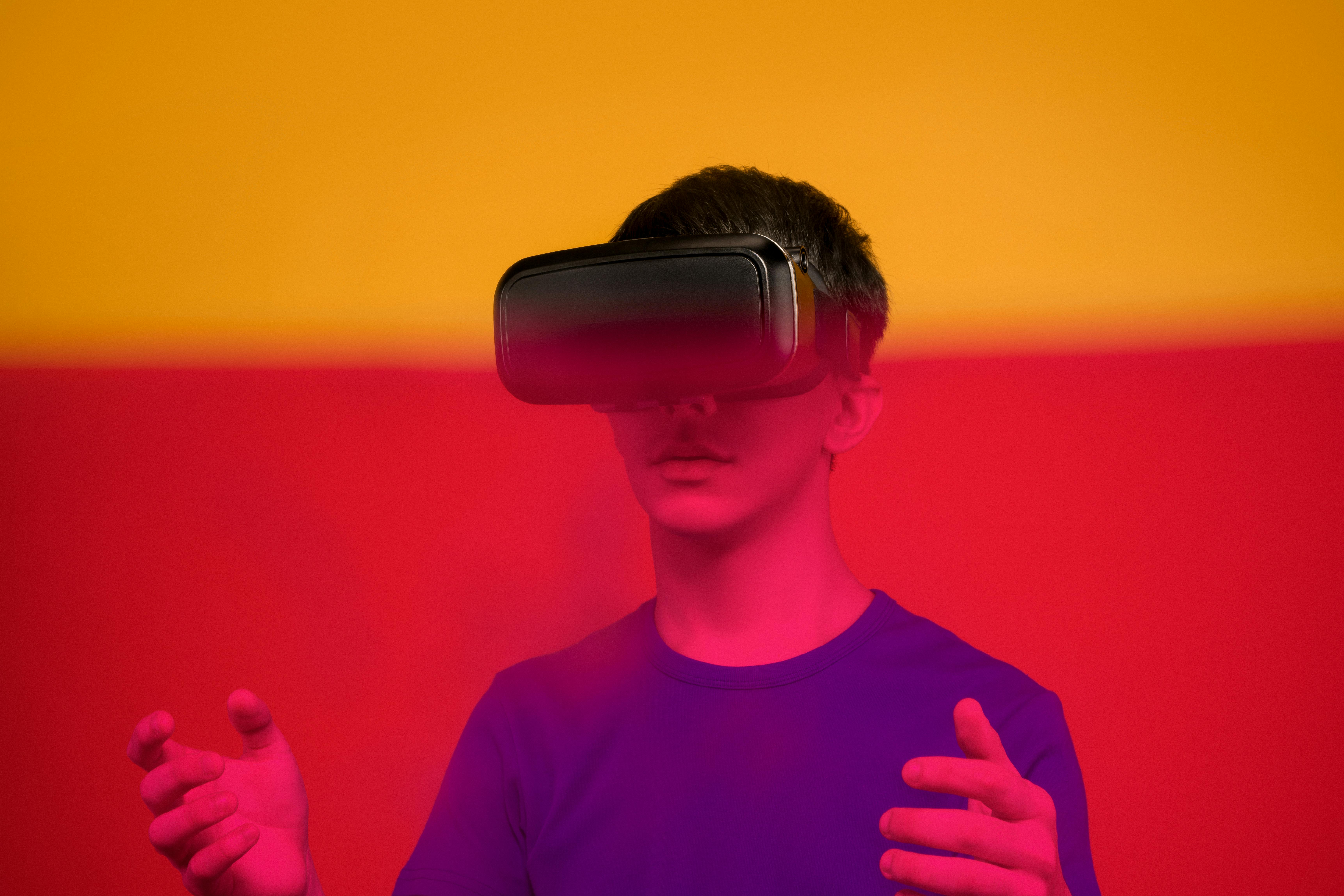 Young person wearing a virtual reality headset with hands raised against a vibrant red and orange background.