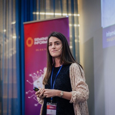 Hombre sonriente con barba y camiseta azul mirando a la cámara sobre fondo gris.