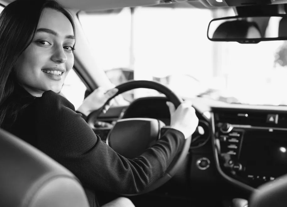 Man smiling enthusiastically with his fist raised while sitting in the driver's seat of a car.