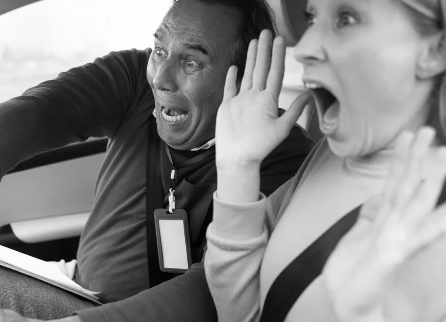 A smiling couple talking with a car salesperson who is holding a brochure and gesturing near a parked car.