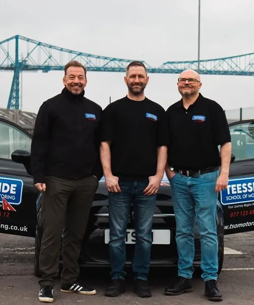 Student celebrating a driving test pass in a branded Teesside School of Motoring vehicle.