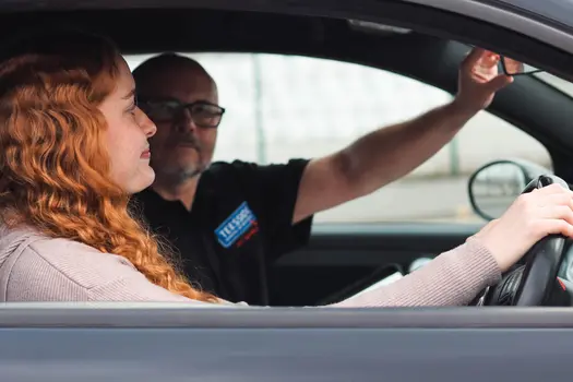 Successful student celebrating a driving test pass in a black Teesside School of Motoring learner vehicle.