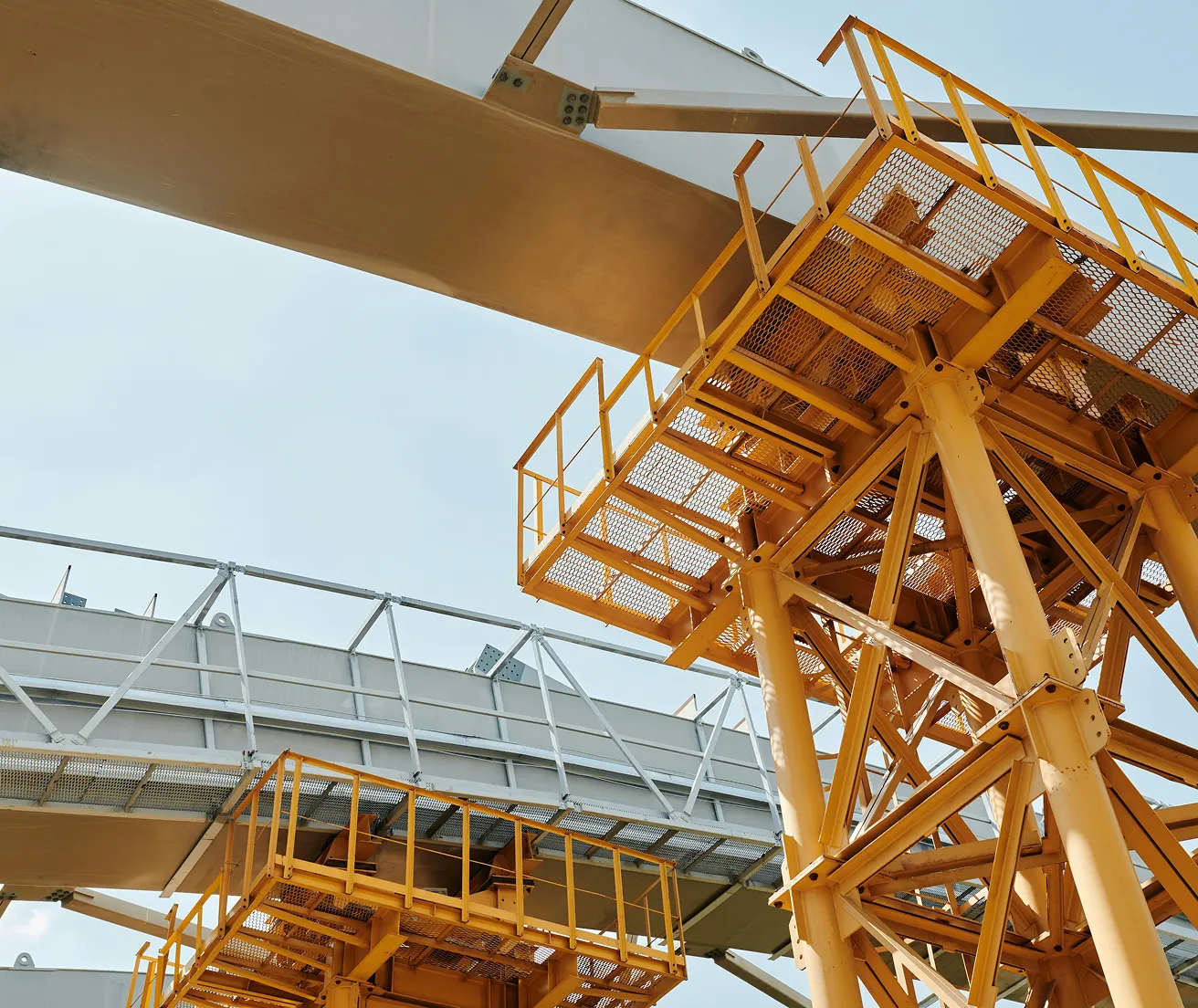 Close-up view of yellow industrial scaffolding and metal walkways against a pale sky.