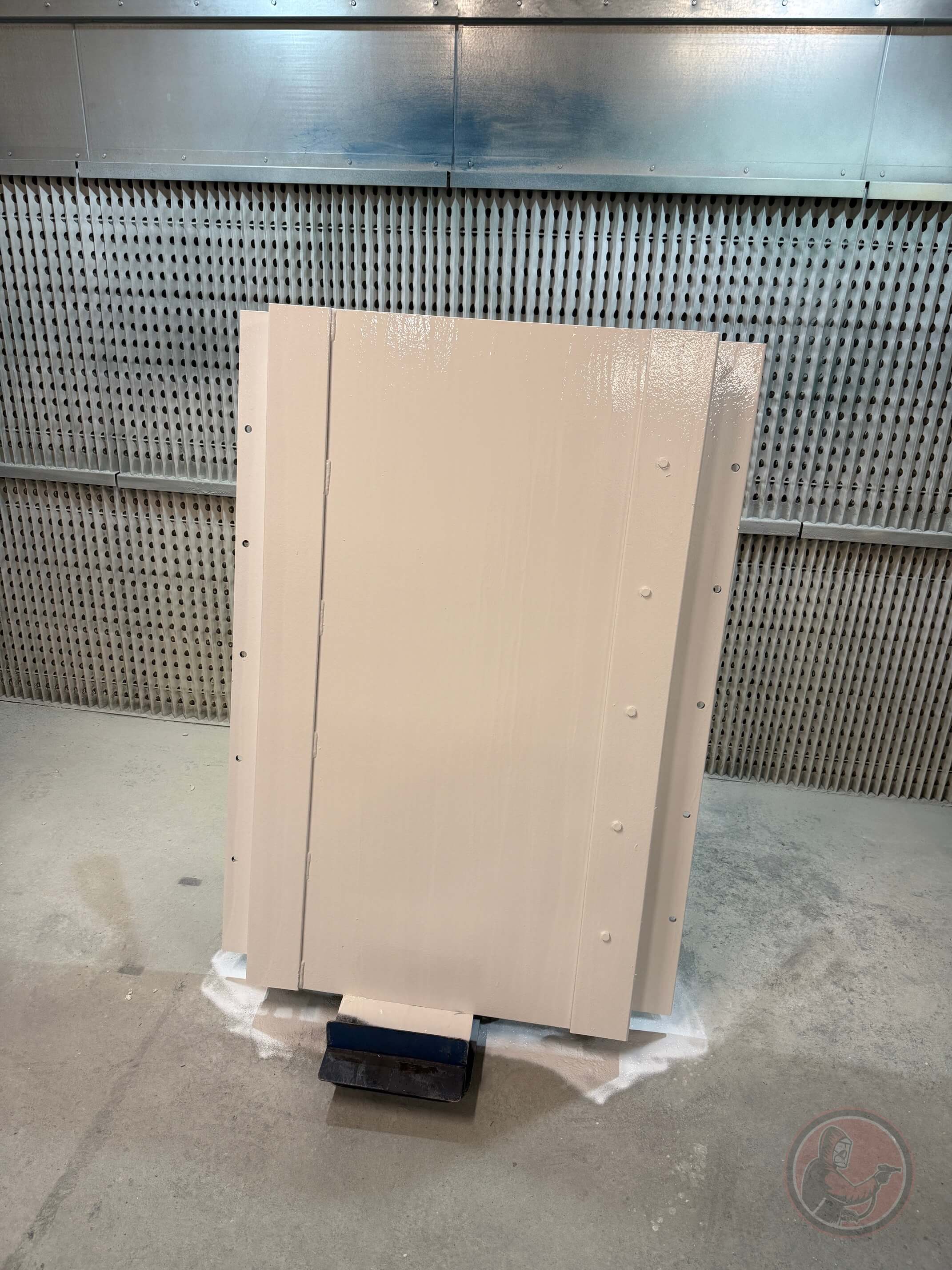 Three beige metal steel panels standing upright on a concrete floor against a perforated industrial metal wall background.