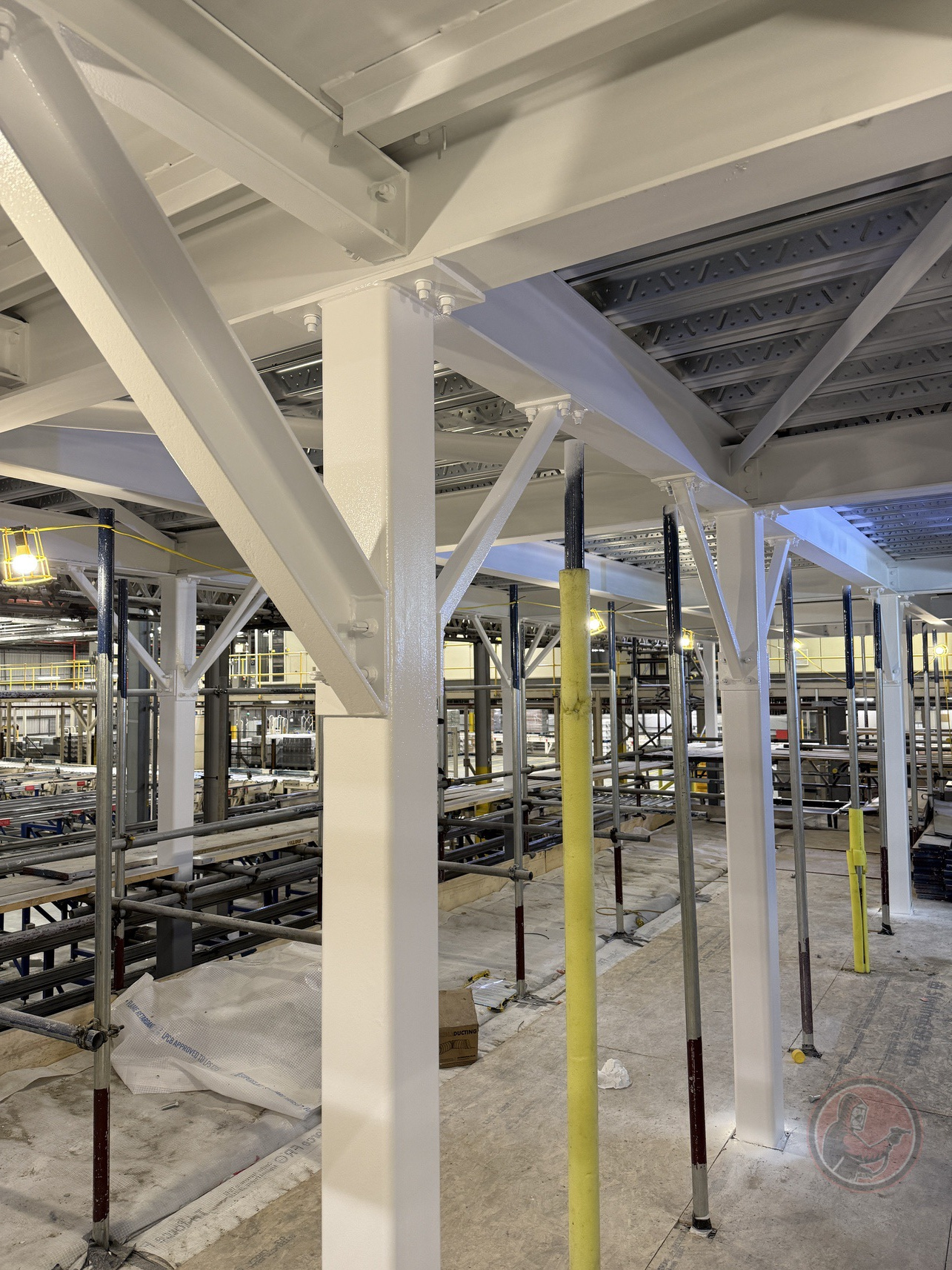 White painted structural steel beams and columns in an indoor construction site with scaffolding and supports.
