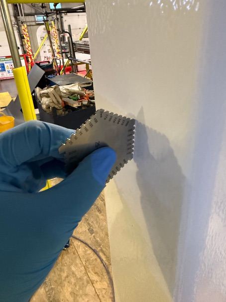 Wet-film thickness gauge checking freshly applied white intumescent coating.