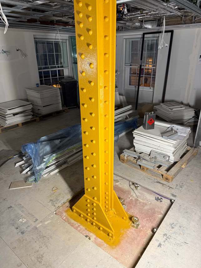 Yellow-primed riveted steel column before intumescent coating.