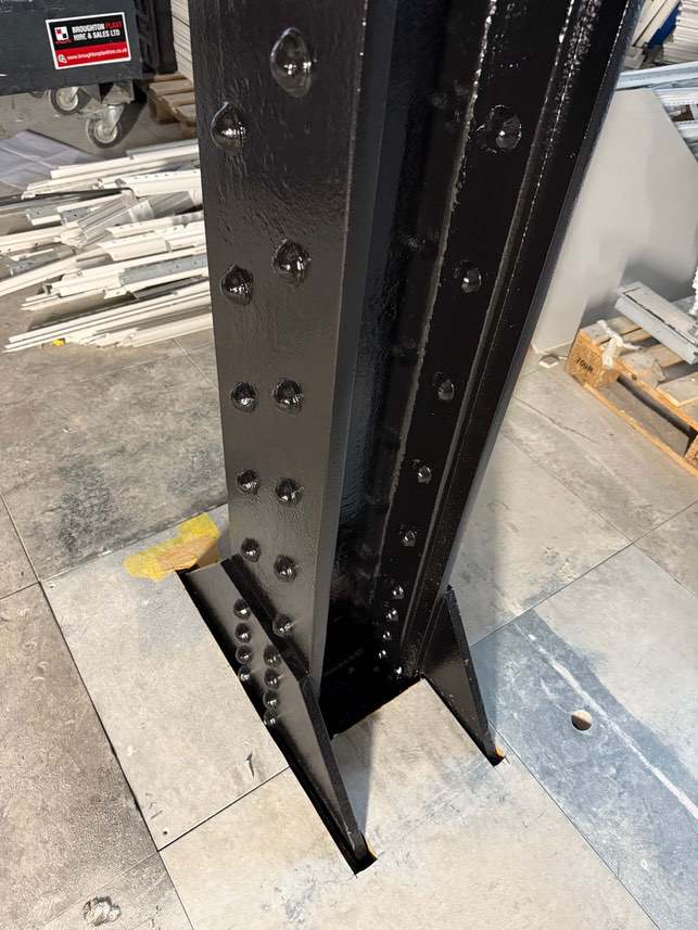 Close-up of the black topcoat on a riveted steel column and base plate.