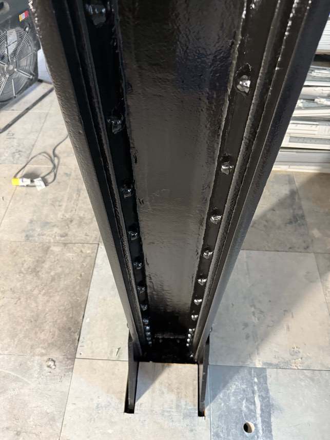Black decorative finish around the base of a riveted steel column.