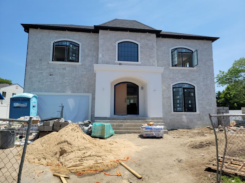 Stone two-story house under construction with open windows, a portable toilet, and building materials in front.