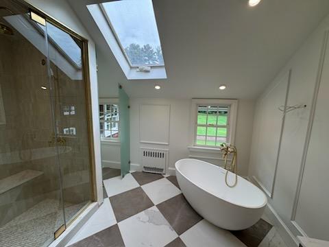 Modern bathroom with black hexagonal tile floor, wooden vanity with white countertop, rectangular mirror, and glass shower enclosure with marble walls.