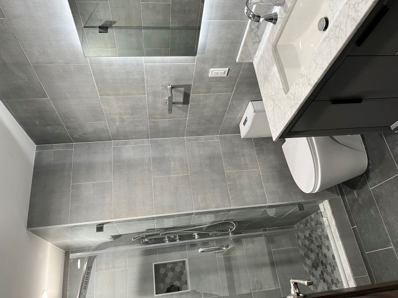 Modern bathroom with a glass-enclosed shower, white toilet, and marble countertop sink with dark cabinetry.